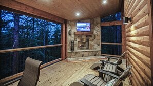 Une terrasse en bois avec une cheminée en pierre et un écran de tél évision.