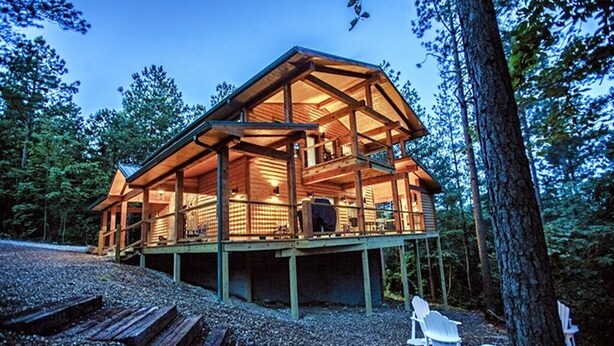 Une cabane en bois dotée d’un balcon, entourée d’arbres.