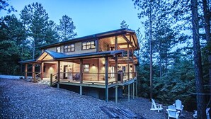 Une cabane en rondins à deux étages, dotée d’une terrasse et entourée d’arbres.