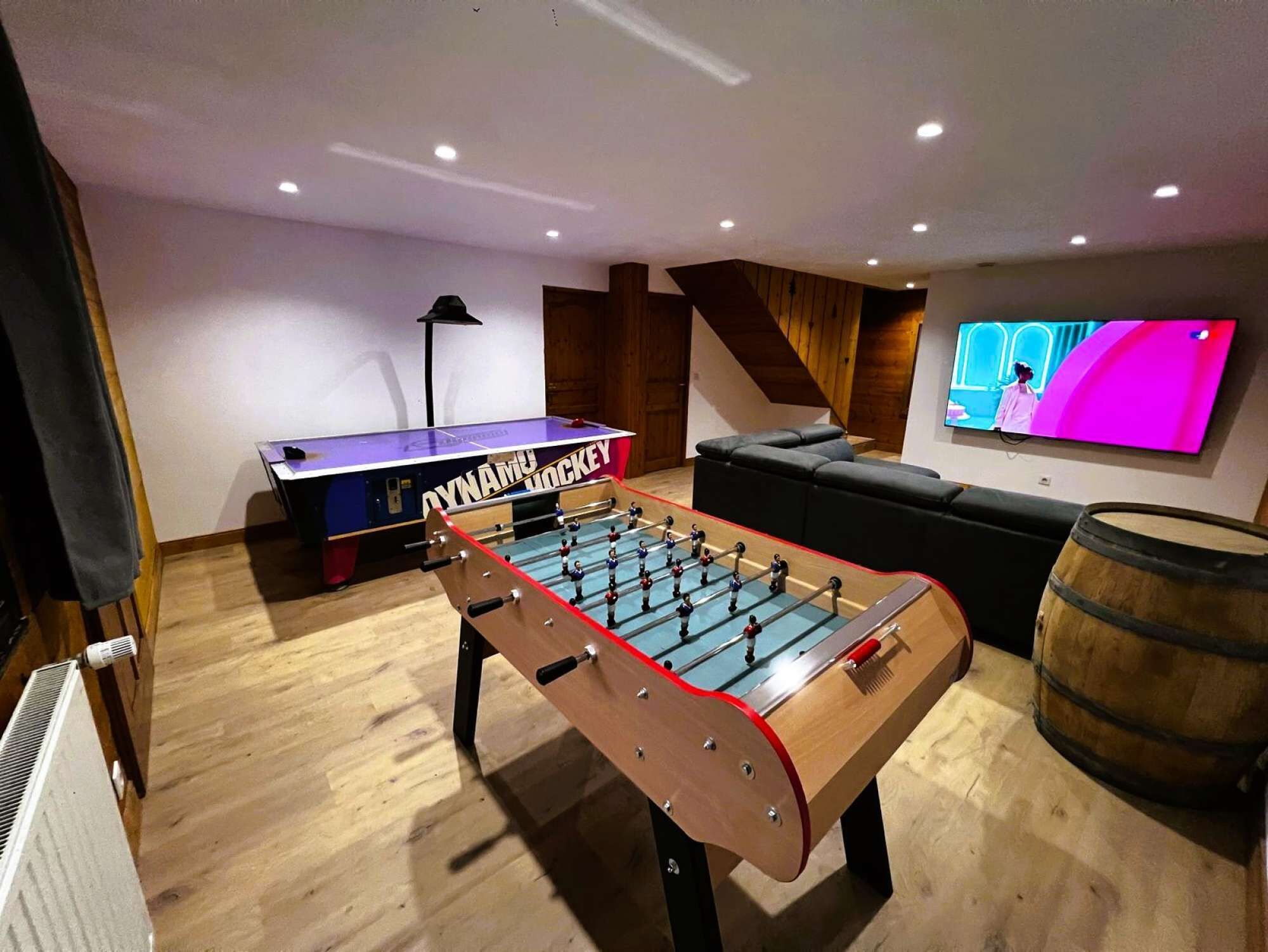 A room with a foosball table, a television, a sofa, and a wooden barrel.