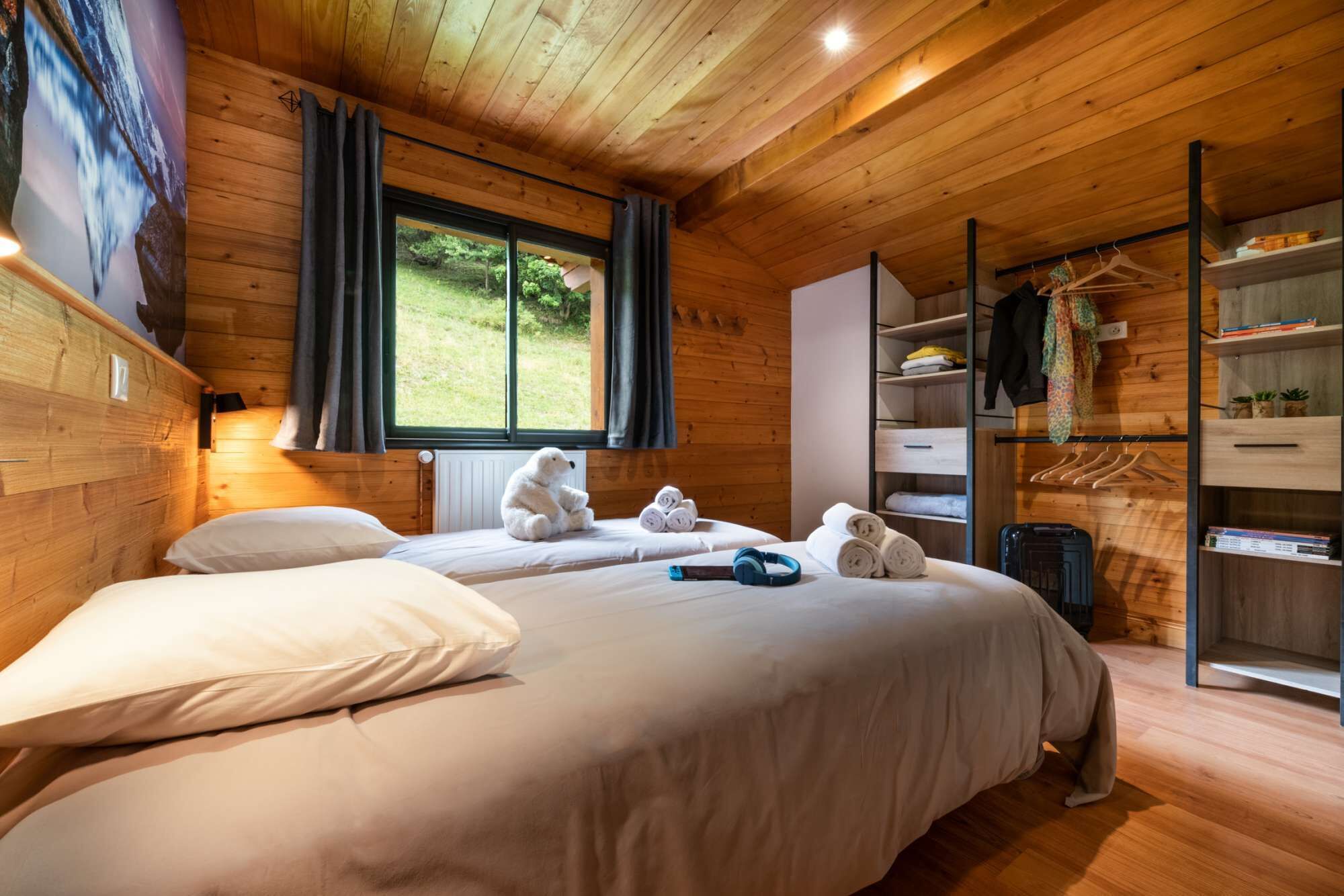 Una habitación acogedora con techo de madera, una cama grande con ropa blanca, una ventana con cortinas y un armario empotrado con espacio para colgar.
