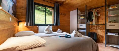 Una habitación acogedora con techo de madera, una cama grande con ropa blanca, una ventana con cortinas y un armario empotrado con espacio para colgar.