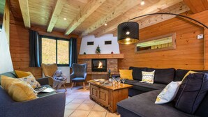 Un salon chaleureux avec une cheminée, des murs en bois et un lustre moderne.