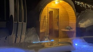 Une cabane en bois avec une entrée en arc de cercle, un jacuzzi à l’avant et de la neige au sol.