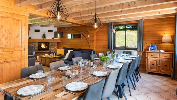 L’intérieur d’un chalet en bois comprend un coin repas, une cheminée et de grandes fenêtres.