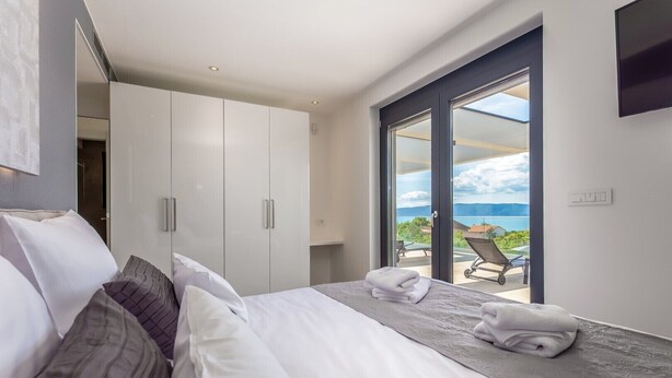 Un dormitorio moderno con una cama grande, un armario y un balcón con vistas al mar.