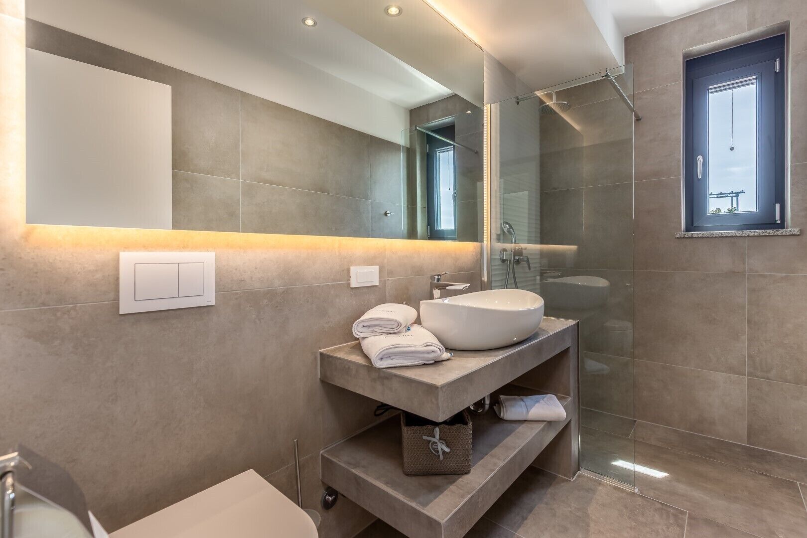 A modern bathroom with a large mirror, a round sink, and a walk-in shower.