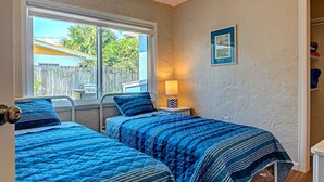 Un dormitorio con dos camas, una ventana, una lámpara de noche y un cuadro en la pared.