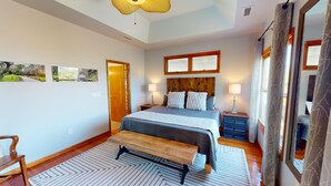 A bedroom with a large bed, two bedside tables, a bench, and a view of the outdoors through the window.