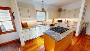 A modern kitchen with white cabinets, a granite countertop, a built-in stove, and a window with blinds.