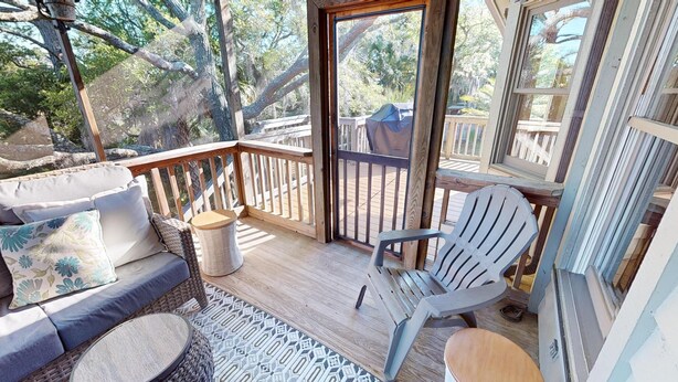 A covered outdoor seating area with a wooden deck, wicker furniture, and a patterned rug.