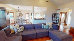 A living room with a sectional sofa, a dining table, and a kitchen area.