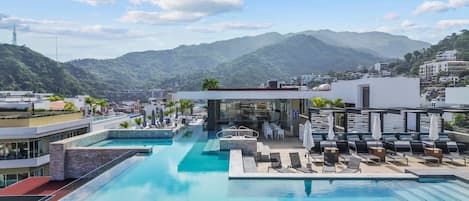 Piscina infinita en la azotea con sillones de descanso y una zona de bar, con vistas a un paisaje montañoso.