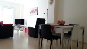 En moderne stue med et fjernsyn, et spisebord med stole og en rød sofa.