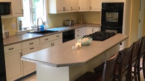 Una cocina con una isla central, armarios blancos, una estufa y un fregadero.