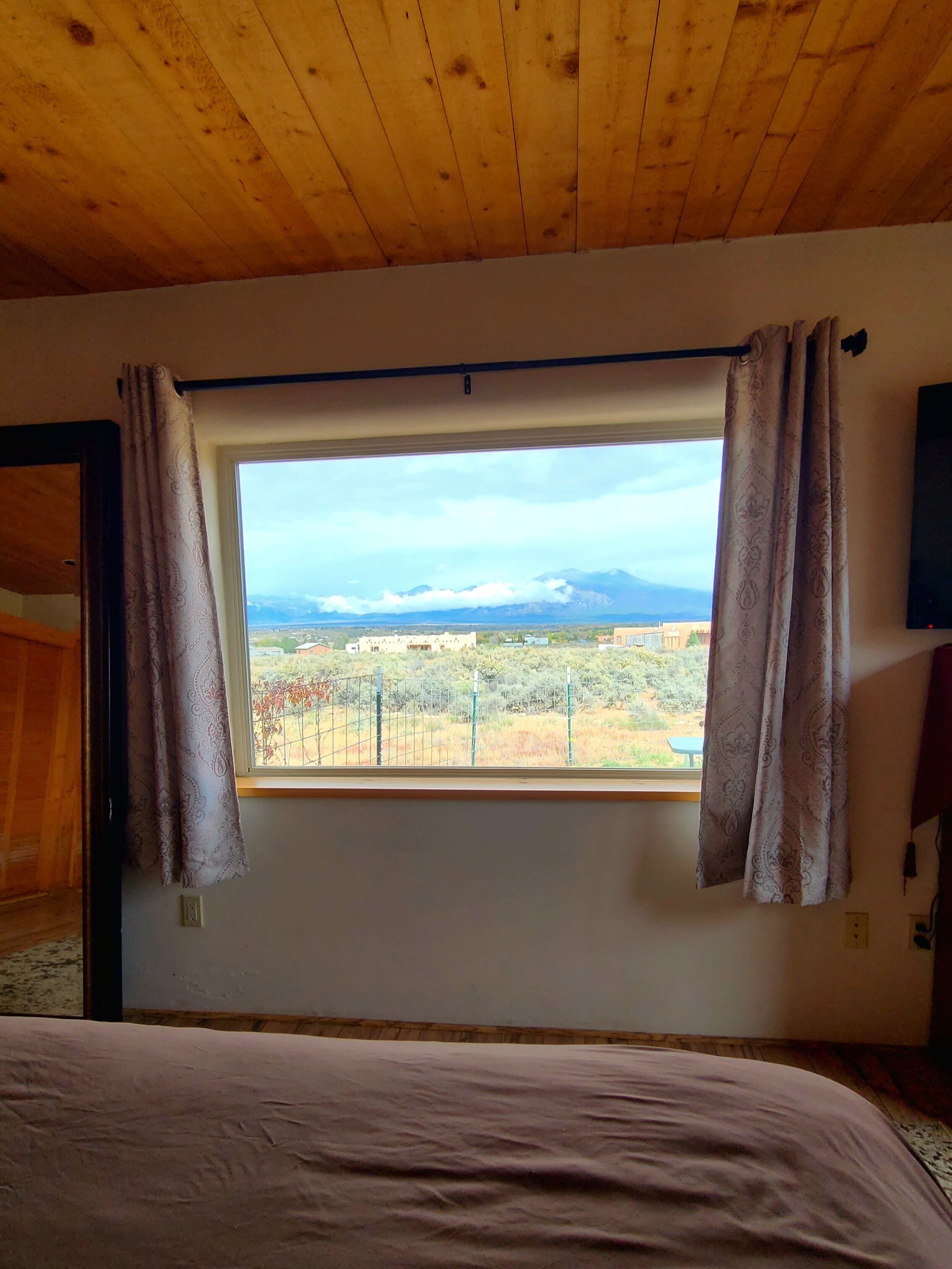 A bedroom with a large window, wooden ceiling, and a bed with a pink bedspread.