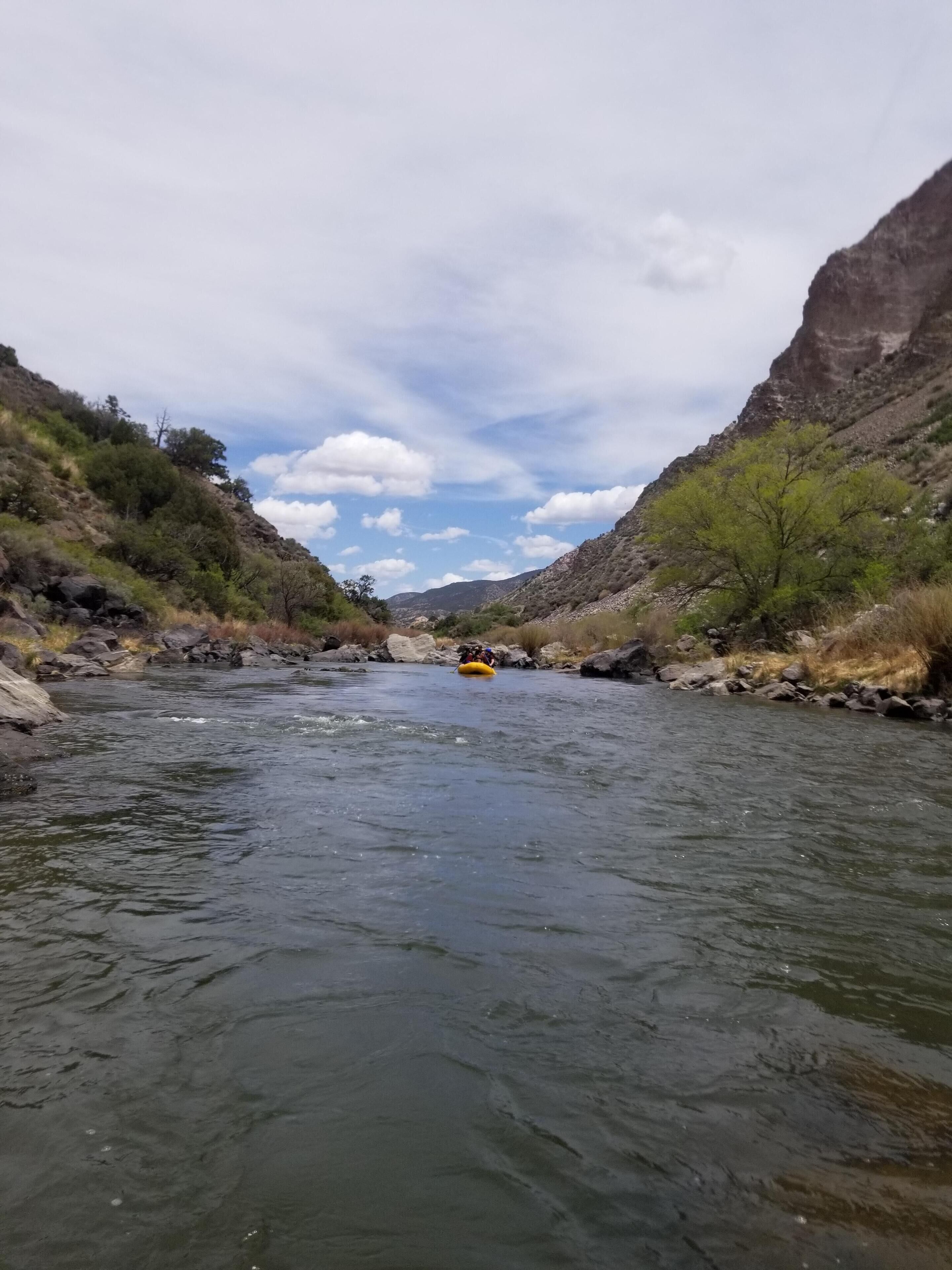 Un río con una balsa en el centro, rodeado de colinas rocosas y vegetación escasa.