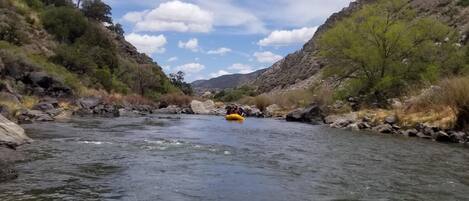 Un río con una balsa en el centro, rodeado de colinas rocosas y vegetación escasa.