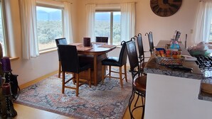 Un coin repas avec une table en bois, des chaises et un lustre. Il y a également un coin cuisine avec une cuisinière et une horloge au mur.