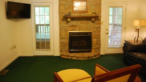A living room with a stone fireplace, a television mounted on the wall, and a green carpet. - The Wildlife Hot Tub Cabin @ LakePointe Resort - no cleaning fees!  (Russell Springs)