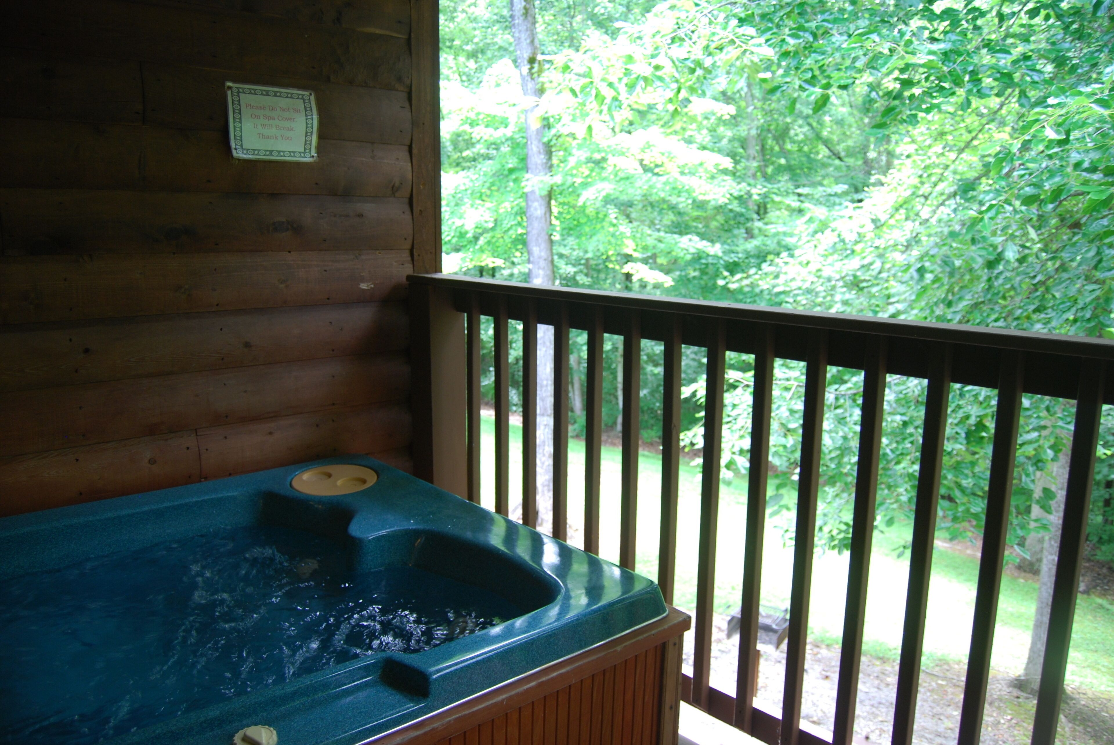 A wooden cabin with a hot tub on a balcony overlooking a forest.