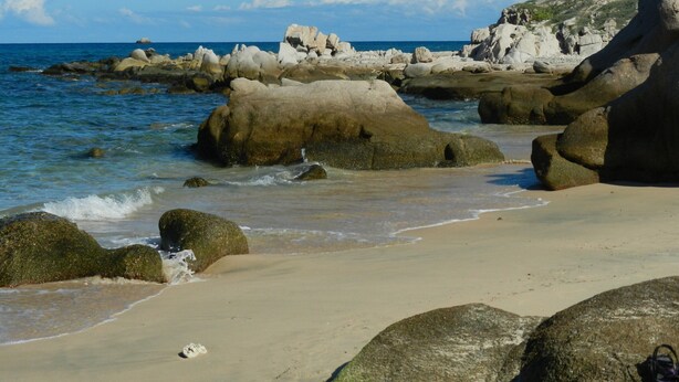 Une plage rocheuse parsemée de gros rochers, avec des vagues douces.