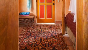 Une pièce avec un tapis à motifs, une porte en bois dotée de panneaux rouges, un lit à baldaquin blanc et un plafond en osier.