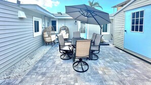 Une terrasse avec des meubles d’extérieur, notamment des chaises et une table, placée sous un grand parasol.