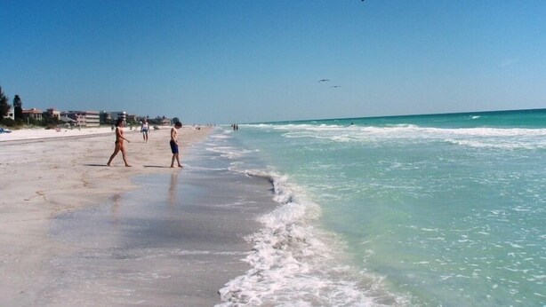 Une plage avec un ciel dégagé, des vagues et des gens qui se promènent.
