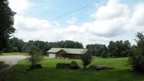 A single-story brick house with a green roof, surrounded by a well-maintained lawn and large rocks.