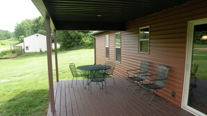 A covered patio with a table and chairs, a grassy yard, and a house in the background.