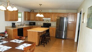 A kitchen with wooden cabinets, a stainless steel refrigerator, a coffee maker, and a dining area with a wooden table and chairs.