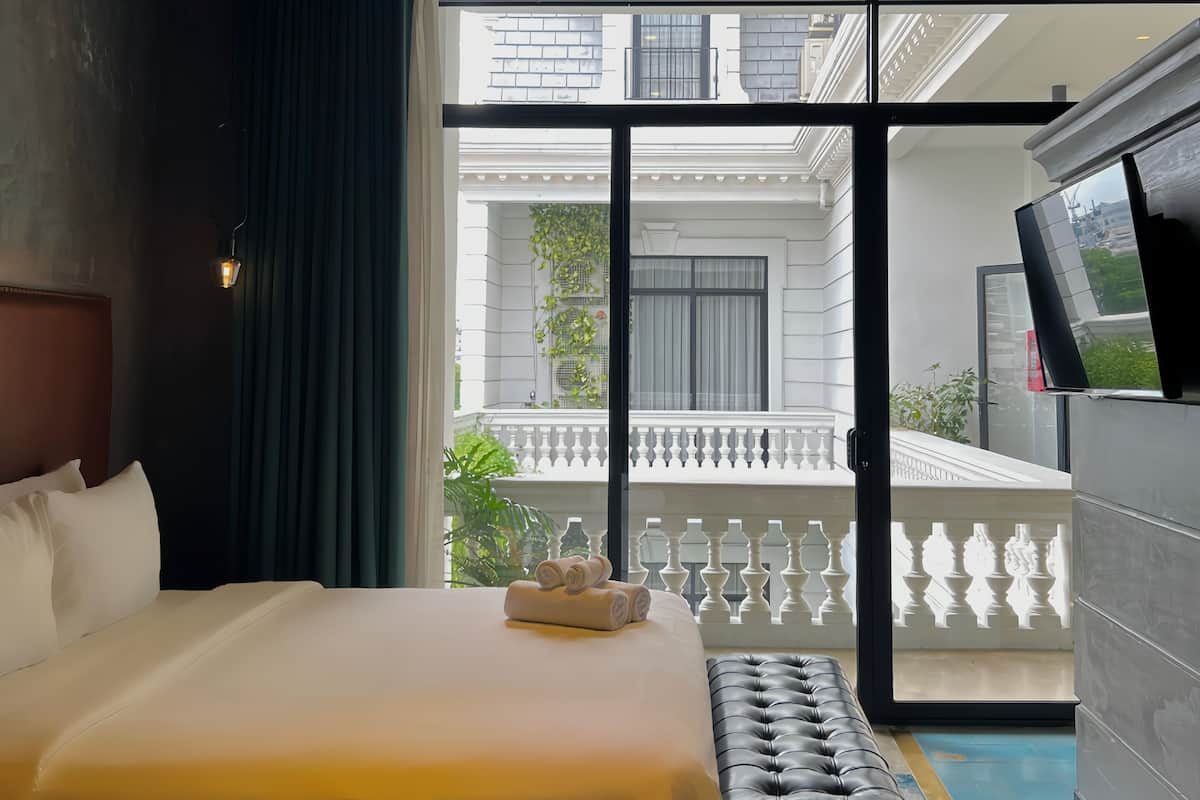 Une chambre d’hôtel avec un grand lit, un banc, une télévision et une vue sur un balcon doté d’une balustrade.