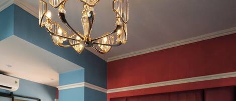 A hotel room with a large bed, a red headboard, a chandelier, and a bathroom visible through an open door.
