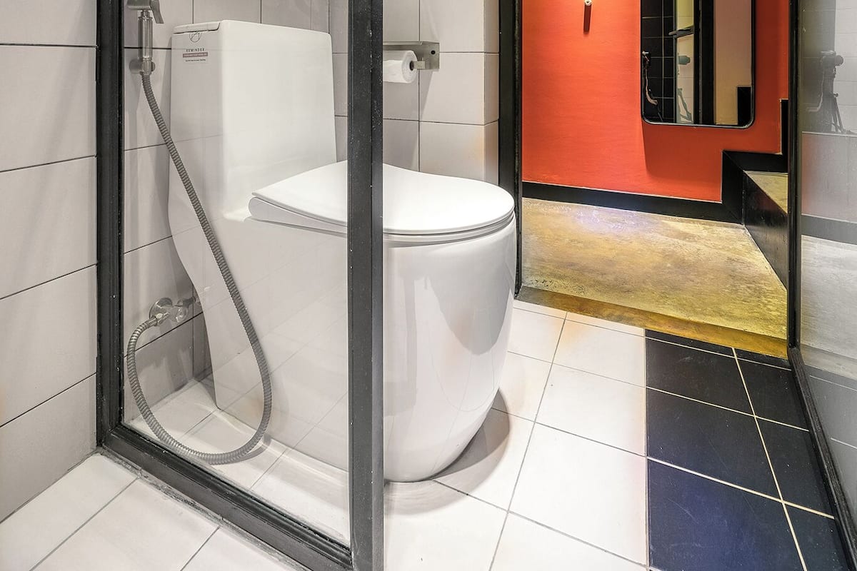 Une salle de bain moderne avec une douche à parois de verre, des toilettes blanches et un mur d’accent rouge.