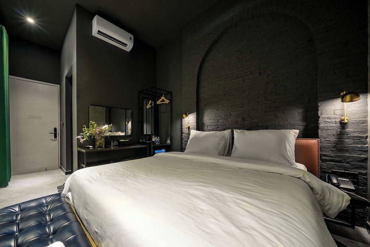 Une chambre moderne avec un grand lit, une commode, un miroir et un mur en pierre.