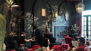 Ein Restaurant mit roten Sitzmöglichkeiten, Wandverzierungen in Schwarz und Gold sowie großen Kübelpflanzen.