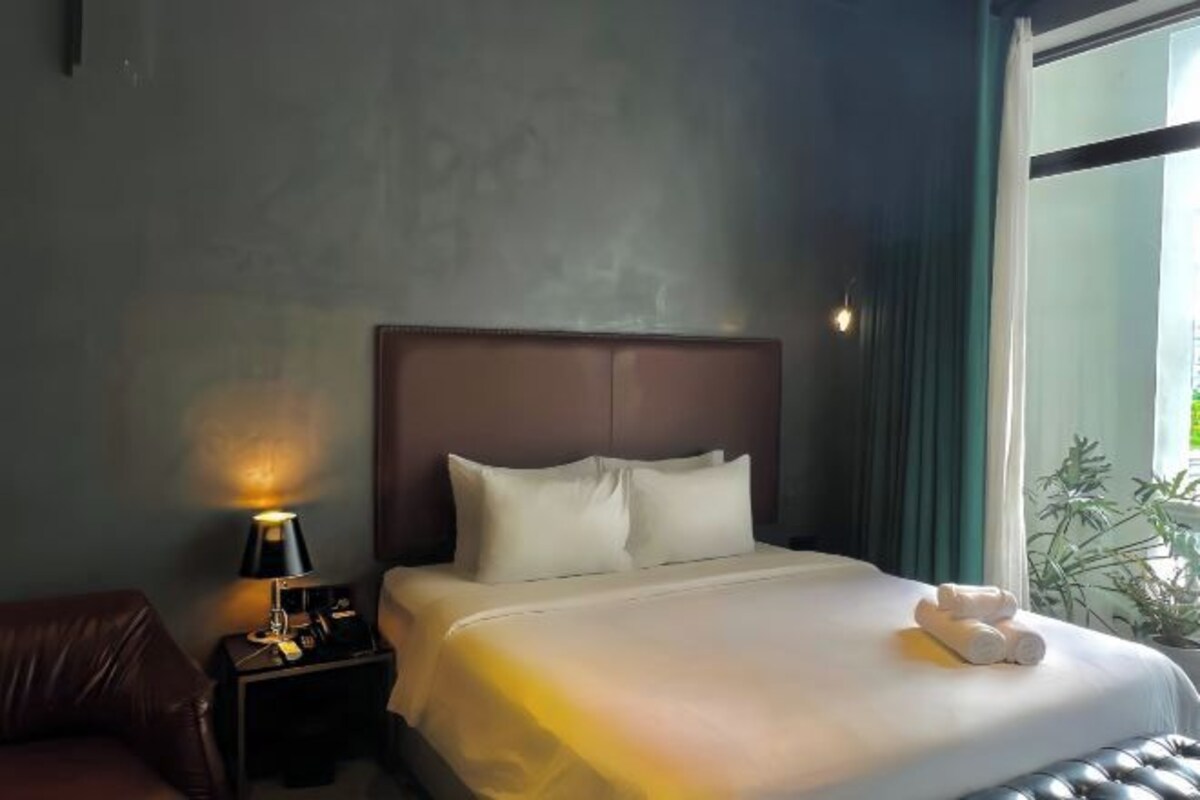Une chambre d’hôtel avec un lit, une table de chevet avec une lampe, une fenêtre avec des rideaux et une vue sur la verdure.
