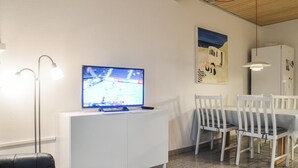 Een moderne woonkamer met een flatscreen-tv, witte meubels en een eethoek met tafel en stoelen.