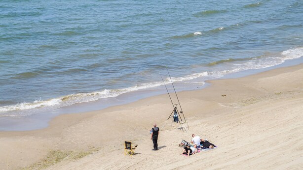 Een strand met een zandstrand, enkele mensen en een hengel.