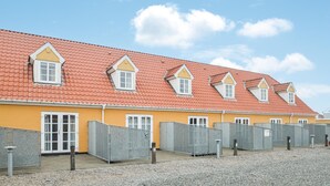 Een rij gelijkvloerse gebouwen met rode dakpannen en gele muren, met meerdere ramen en afgesloten ruimtes, waarschijnlijk voor tijdelijke verblijven.