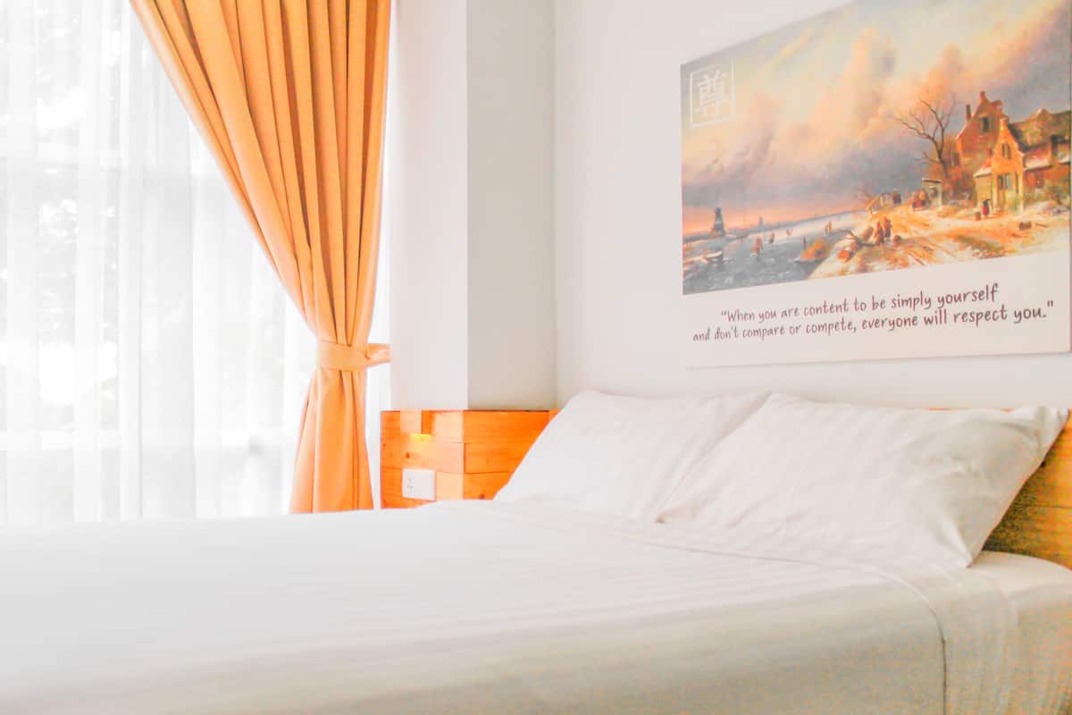 A hotel room with a bed, curtains, a painting, and a quote on the wall.