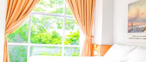 A bedroom with a large window, curtains, a bed, and a wall with a framed picture.