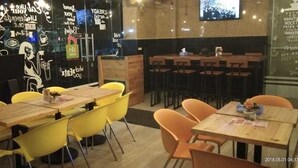 A restaurant with wooden tables and yellow chairs, a counter with a menu, and a wall with various writings and drawings. - An Hotel Satrio Kuningan (Jakarta)