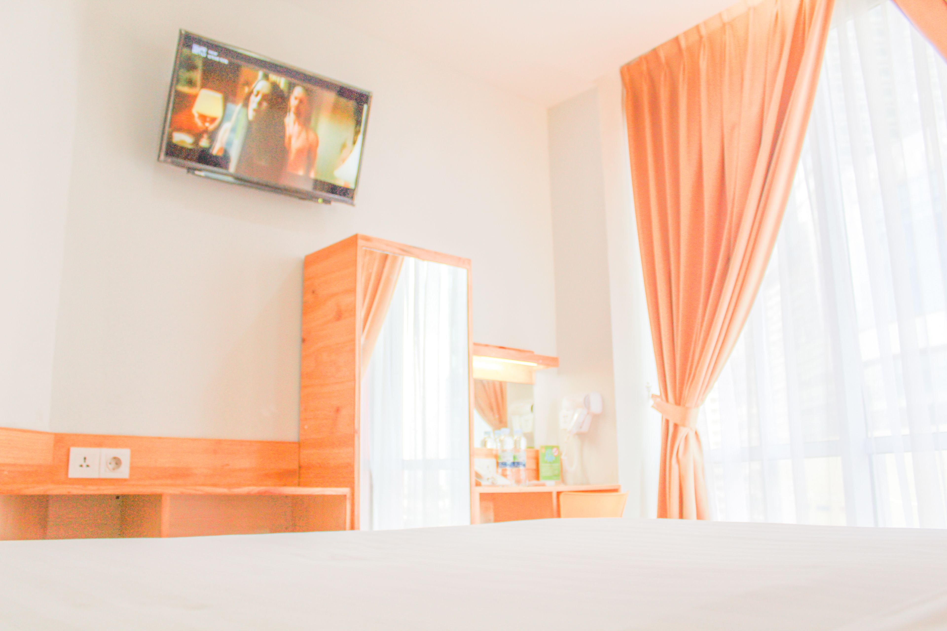 Een hotelkamer met een bed, een aan de muur bevestigde televisie, een houten kast en een raam met gordijnen.