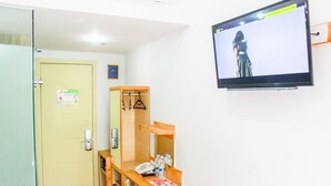 A hotel room with a wooden desk, a chair, a television mounted on the wall, and a door with a sign. - An Hotel Satrio Kuningan (Jakarta)