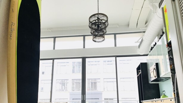 A spacious living area with a large window, a sofa, a chandelier, and a kitchenette.