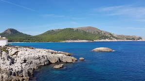 Un paysage côtier caractérisé par un terrain rocheux, une mer bleue et limpide, et une colline couverte d’une végétation dense.