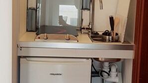 Une cuisine compacte dotée d’un évier encastré, d’un petit réfrigérateur et d’une étagère où sont rangés la vaisselle et les verres.