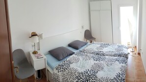 Une chambre à coucher comprenant un lit, une table de chevet, une lampe, une chaise, une armoire et une vue sur l’extérieur.
